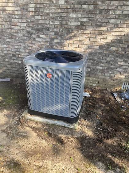 Rheem AC condenser unit installed against a stone home exterior